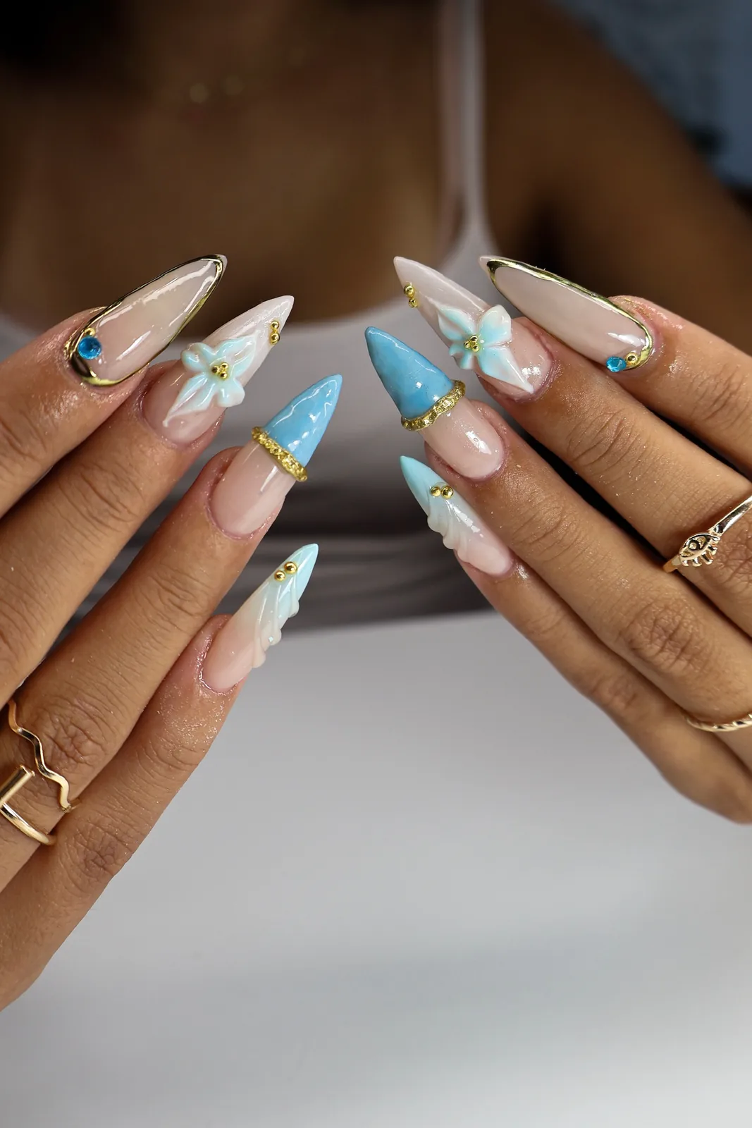 Blue jelly stiletto nails with 3D flowers, gold chrome bands, and gem accents