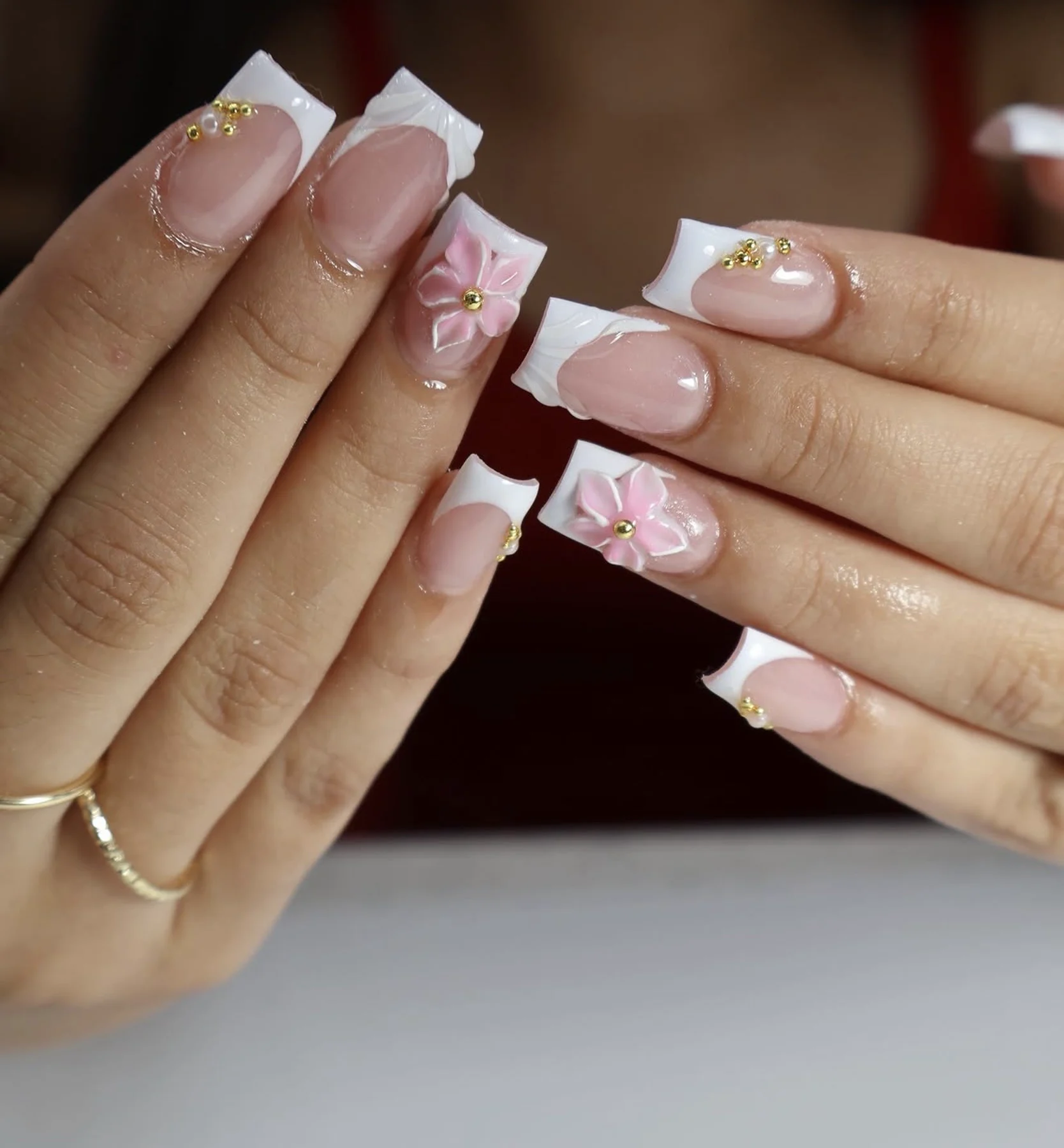 White French square nails with sculpted pink 3D flowers and gold charms