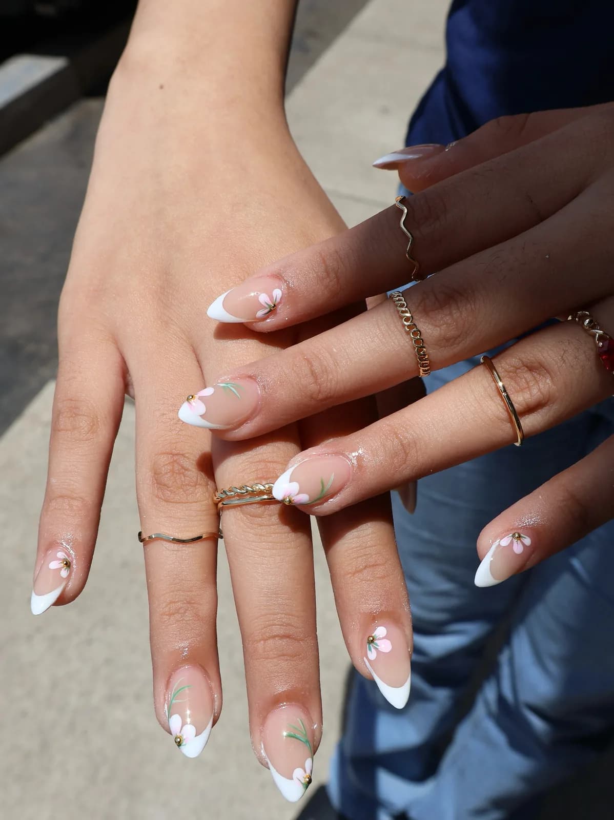 White French tip nails with hand-painted leaf accents in outdoor light
